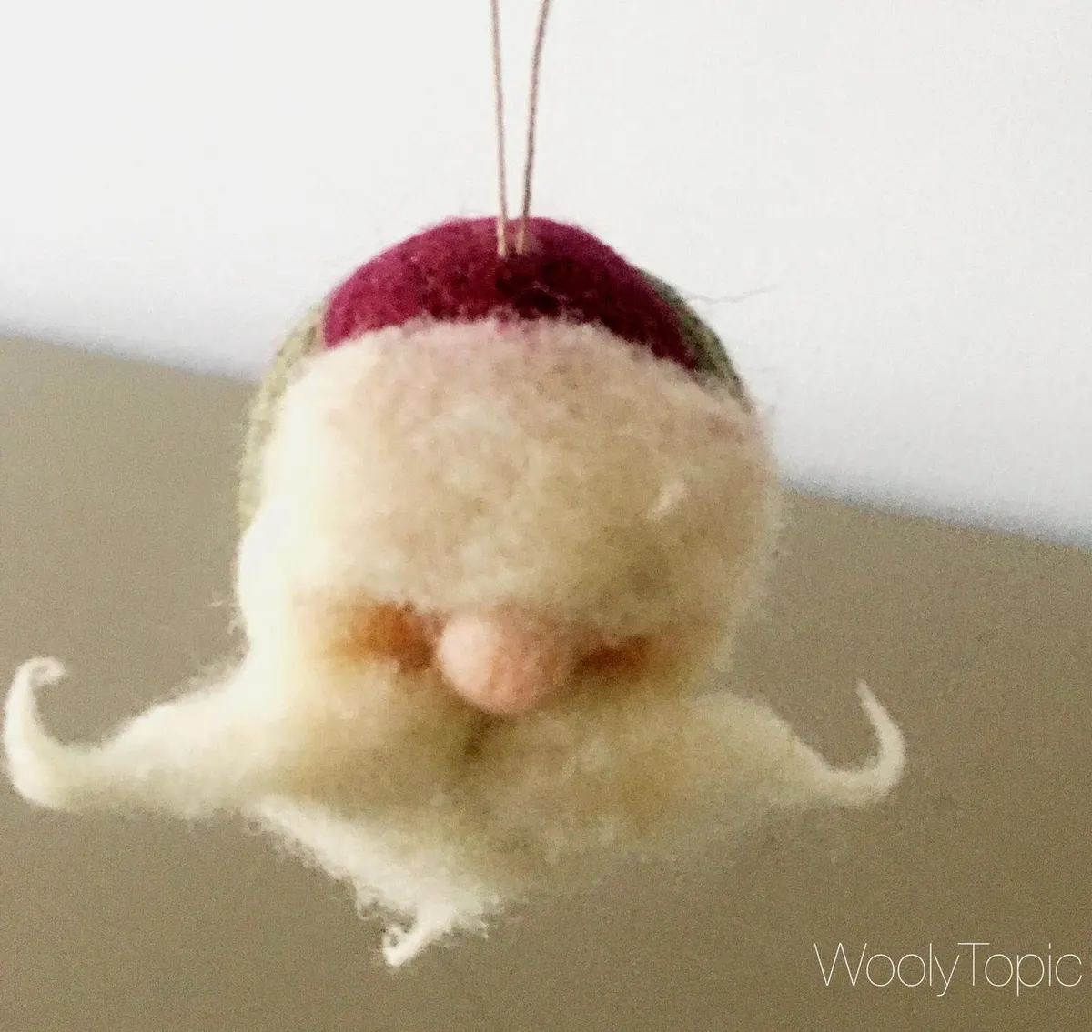 The Santa ornament hanging by its wire hook, red hat and full white beard.