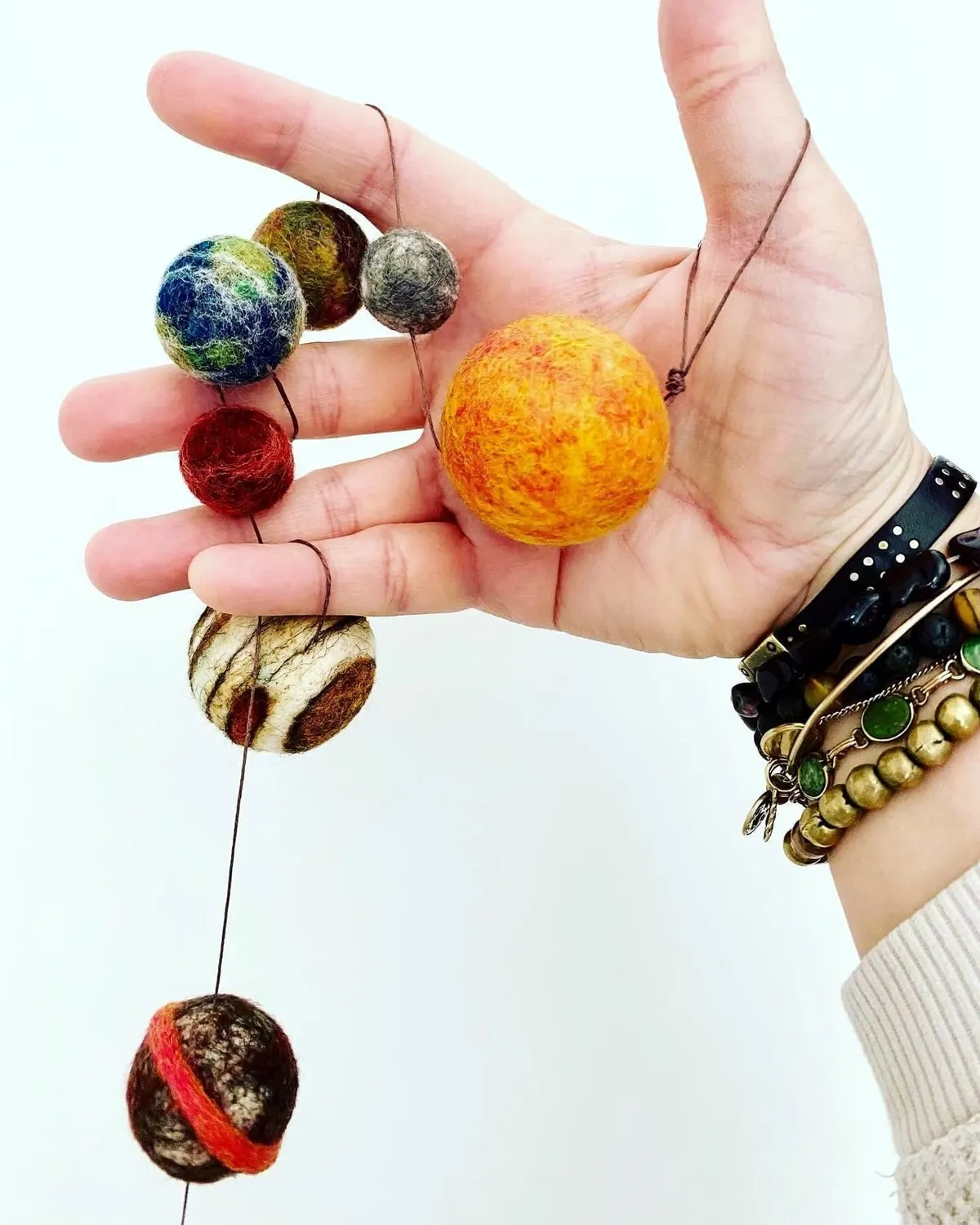 A hand holding the garland up, planets threaded on cord and hanging in a line.